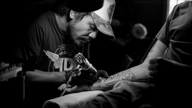 Tattoo & piercing randevu uygulaması. Adam müşterisinin koluna dövme yapıyor.